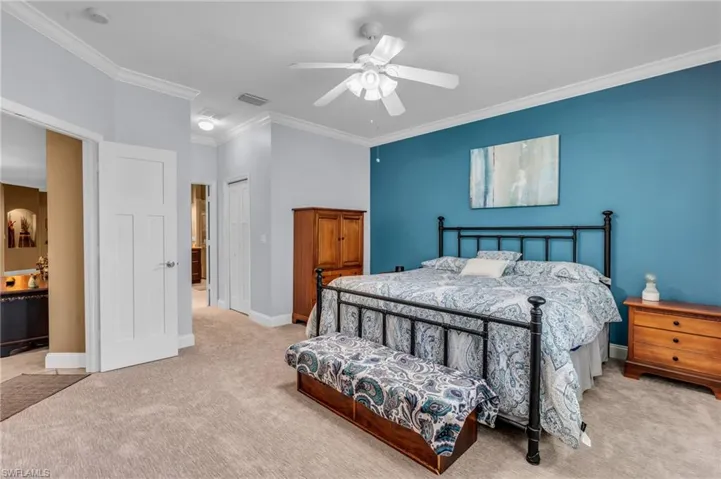 Carpeted bedroom featuring ensuite bath, crown molding, ceiling fan, and a closet