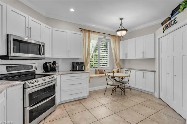 Kitchen with appliances with stainless steel finishes, hanging light fixtures, ornamental molding, and white cabinets