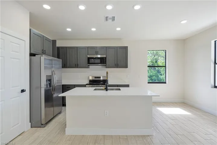 Kitchen with stainless steel appliances, light wood-style flooring, light countertops, an island with sink, and recessed lighting