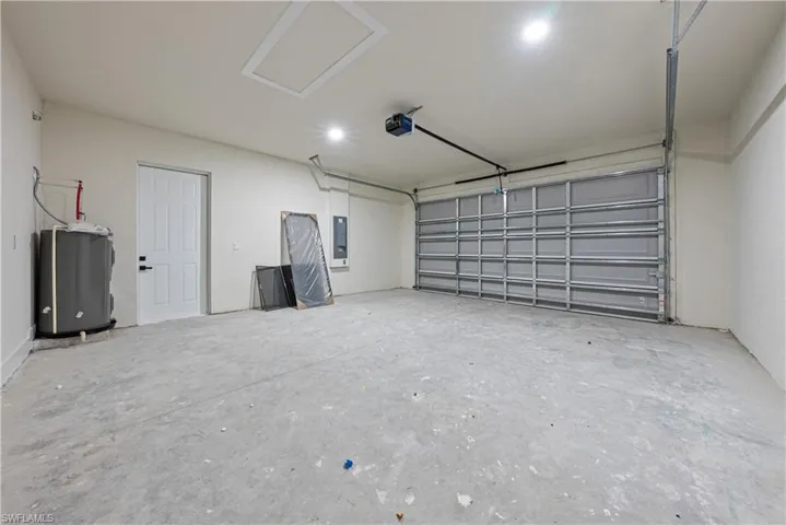 Garage featuring electric panel, a garage door opener, and water heater