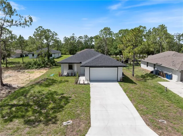 Ranch-style home featuring driveway, a shingled roof, an attached garage, a front lawn, and stucco siding