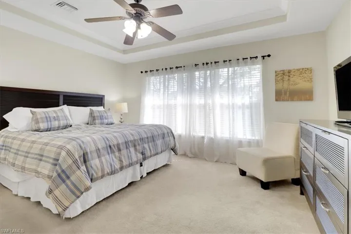Bedroom with a tray ceiling, light colored carpet, and ceiling fan