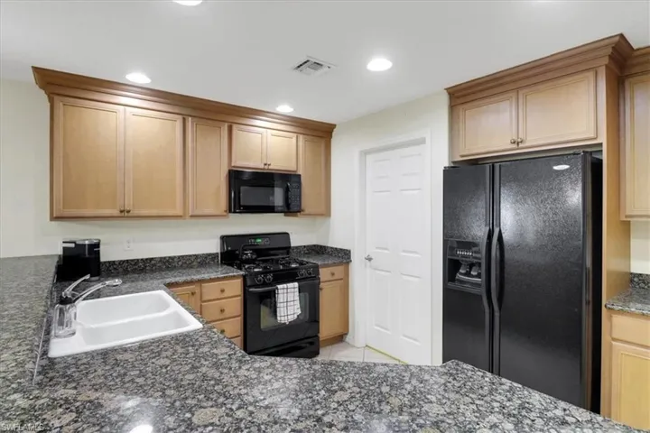 Kitchen featuring black appliances, recessed lighting, light tile patterned flooring, dark stone counters, and light brown cabinets