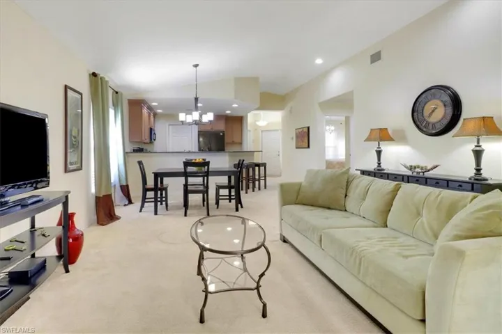 Living room with recessed lighting, light carpet, lofted ceiling, and a chandelier