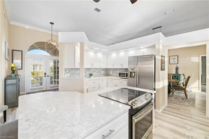 Kitchen featuring appliances with stainless steel finishes, hanging light fixtures, decorative backsplash, light wood-type flooring, and white cabinetry
