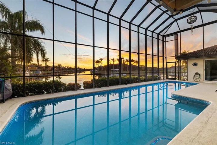 Pool at dusk with a water view and glass enclosure