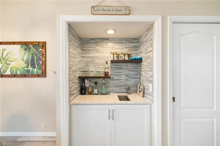Bar with decorative backsplash, sink, white cabinetry, and light wood-type flooring