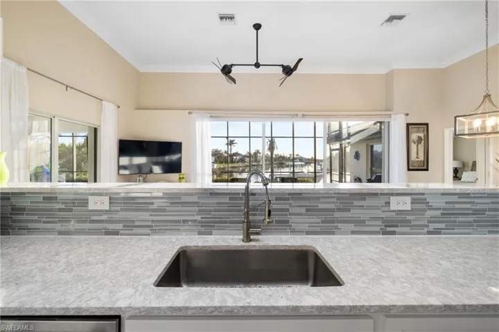 Kitchen with sink, decorative light fixtures, crown molding, light stone countertops, and decorative backsplash