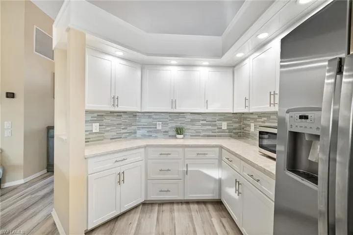 Kitchen with crown molding, white cabinetry, stainless steel appliances, and light stone countertops