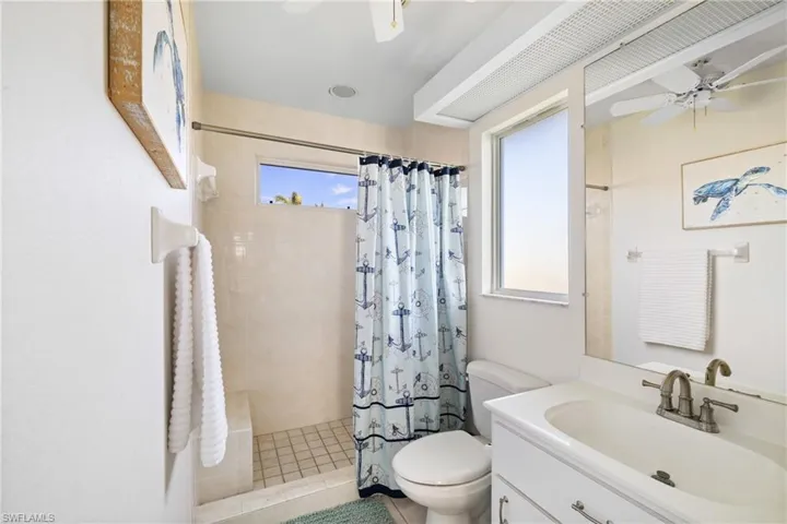 Bathroom featuring toilet, vanity, a shower with shower curtain, and ceiling fan