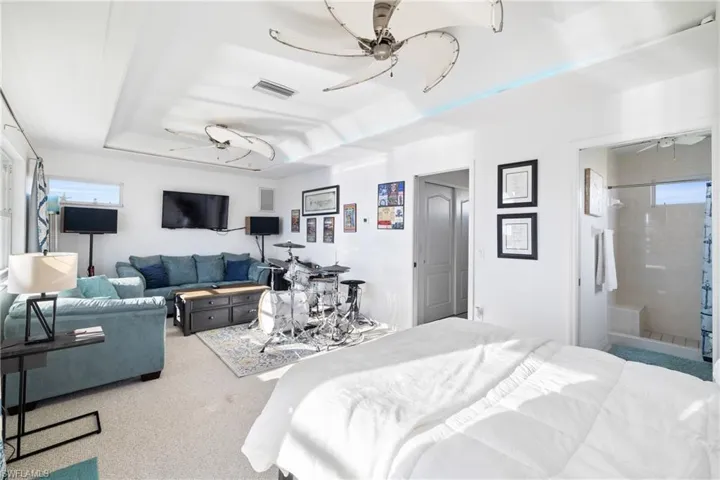 Carpeted bedroom with a raised ceiling, ceiling fan, and connected bathroom
