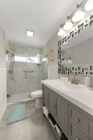 Full bath with a marble finish shower, vanity, a decorative wall, and a wainscoted wall