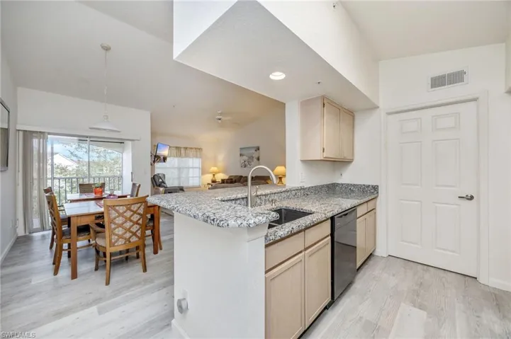 Kitchen featuring light wood finish cabinetry, a peninsula, light stone countertops, light wood finished floors, and lofted ceiling