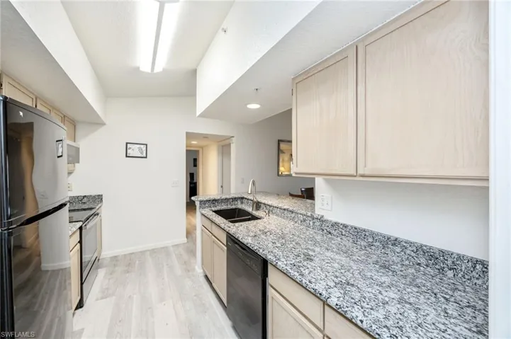 Kitchen featuring light wood finish cabinets, black appliances, light stone counters, a peninsula, and light wood-style floors