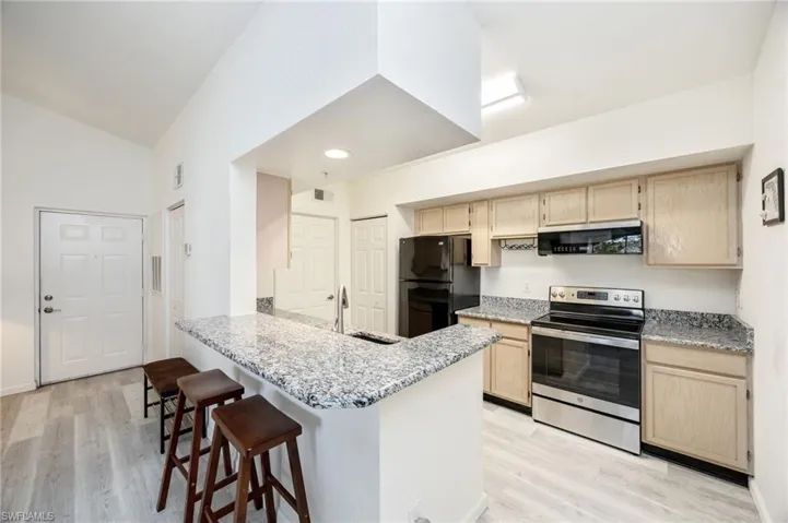Kitchen with light wood finish cabinetry, stainless steel electric range, a breakfast bar area, light stone counters, and freestanding refrigerator