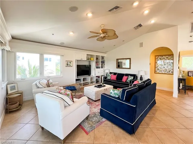 Tiled living room featuring lofted ceiling, built in shelves, and ceiling fan