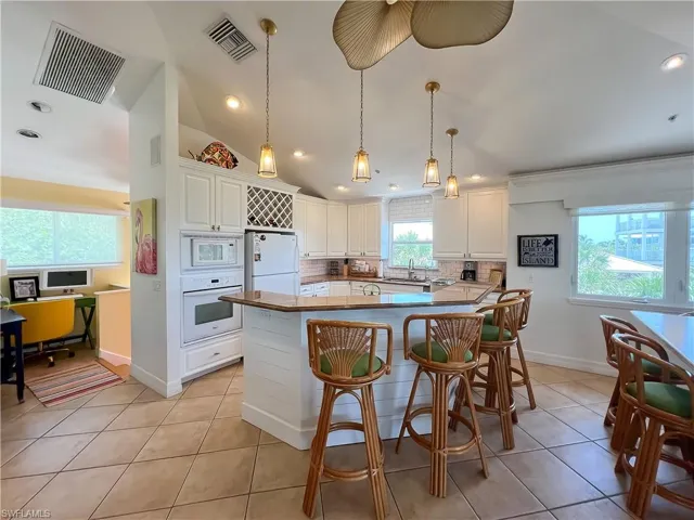 Kitchen featuring light tile flooring, tasteful backsplash, white cabinets, and white appliances
