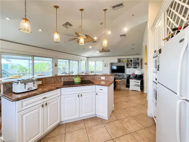 Kitchen with decorative light fixtures, ceiling fan, white cabinetry, and white appliances