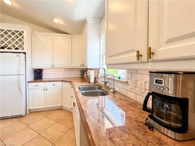 Kitchen with backsplash, sink, white cabinetry, and white fridge