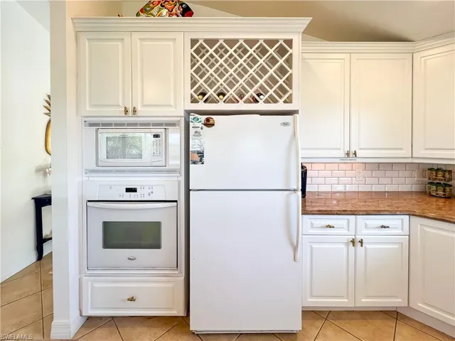 Kitchen featuring white appliances, tasteful backsplash, white cabinetry, and light tile floors