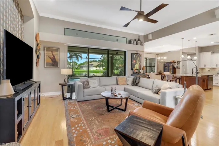 Living room with ceiling fan with notable chandelier, light hardwood / wood-style flooring, and ornamental molding