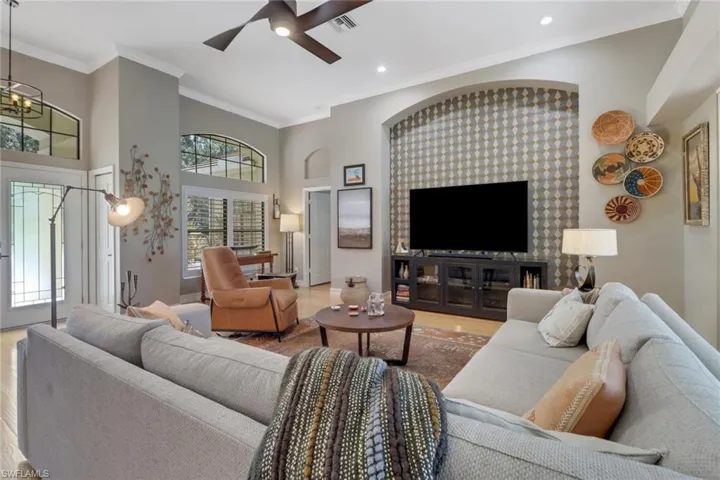 Living room featuring wood-type flooring, ceiling fan with notable chandelier, and crown molding