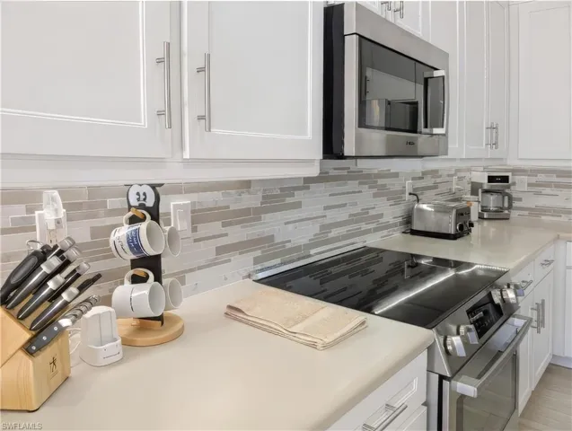Kitchen with backsplash, white cabinets, and stainless steel appliances