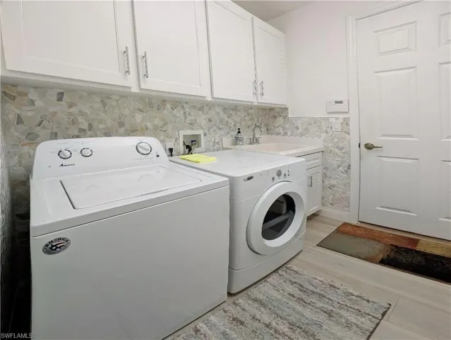 Clothes washing area featuring washer and dryer, light composite flooring, cabinets, and sink