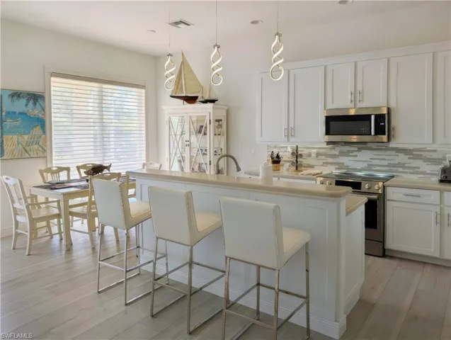 Kitchen with white cabinets, decorative light fixtures, stainless steel appliances, and an island with sink