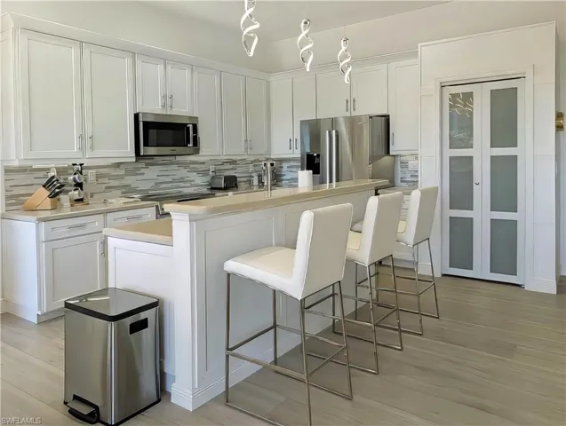 Kitchen with white cabinetry, decorative backsplash, a breakfast bar, a center island with sink, and appliances with stainless steel finishes
