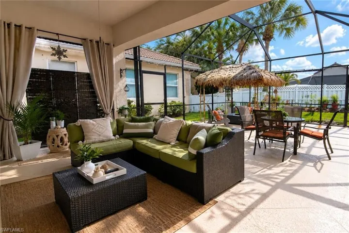 Screened-in outdoor living space featuring textured flooring, a covered patio area, and a thatched umbrella