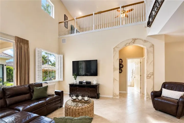 Living area featuring a high vaulted ceiling with clerestory windows, tile flooring, window with plantation shutters, and an arched entryway