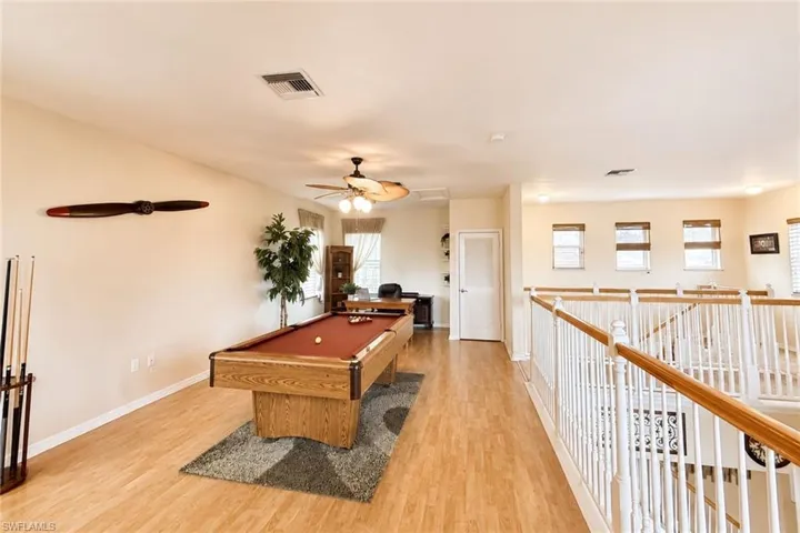 Spacious loft area featuring wood-finish flooring, a ceiling fan with light fixture, and white painted balusters with a wood handrail