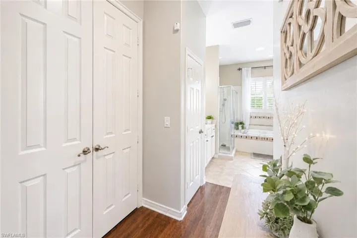 Wood-finish flooring leading into a tiled bathroom featuring a built-in soaking tub, glass-enclosed shower, and plantation shutters