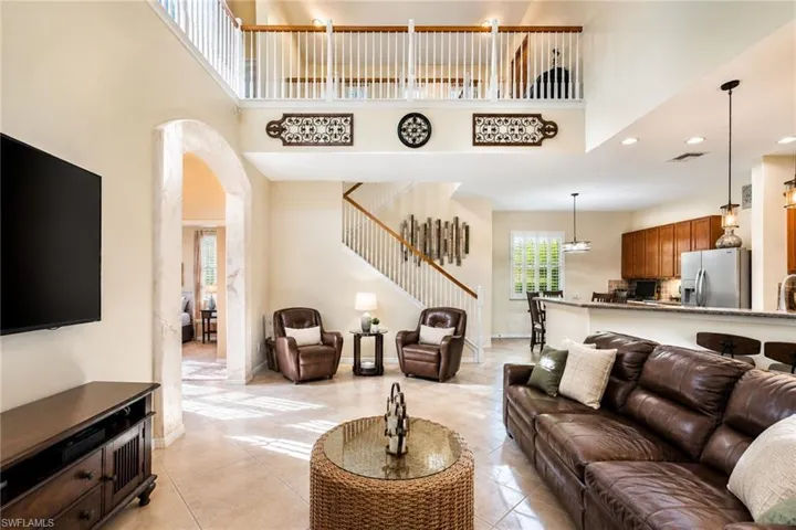Two-story open concept living area featuring a loft, an arched entryway, tile flooring, and a kitchen with warm wood cabinetry