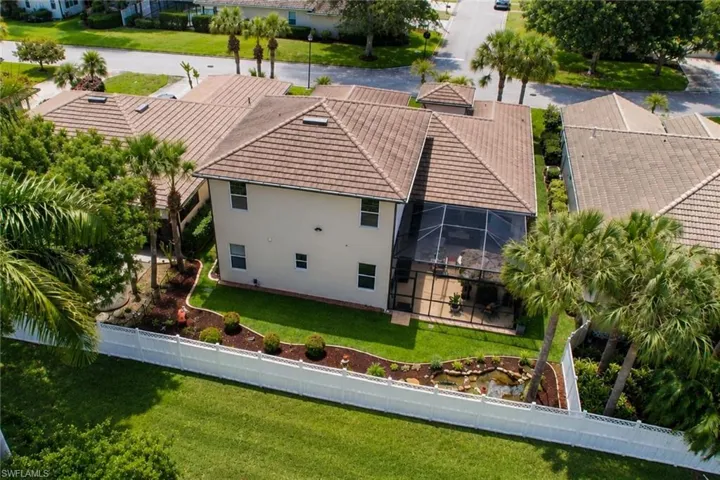 Rear exterior featuring a screened-in patio, mature palm trees, manicured landscaping, and a privacy fence