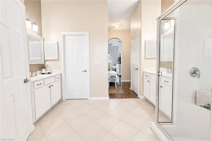 Spacious bathroom featuring diagonal tile flooring, dual vanities with white cabinetry and integrated sinks, a walk-in shower with a built-in bench, and multiple panel doors