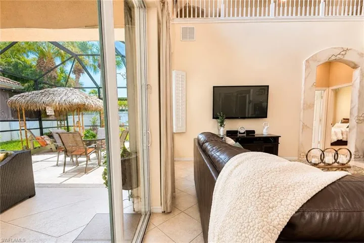 Expansive screened patio featuring a tiki hut, outdoor seating, and mature palm trees