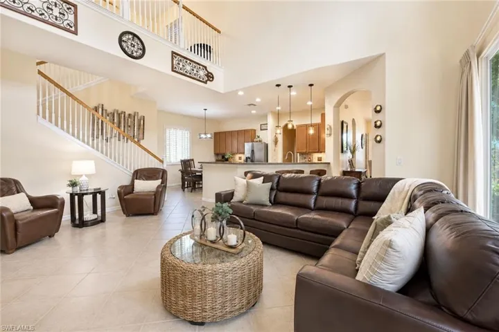 Spacious living area featuring high vaulted ceilings, light tile flooring, and a prominent staircase with white balusters and wood handrails