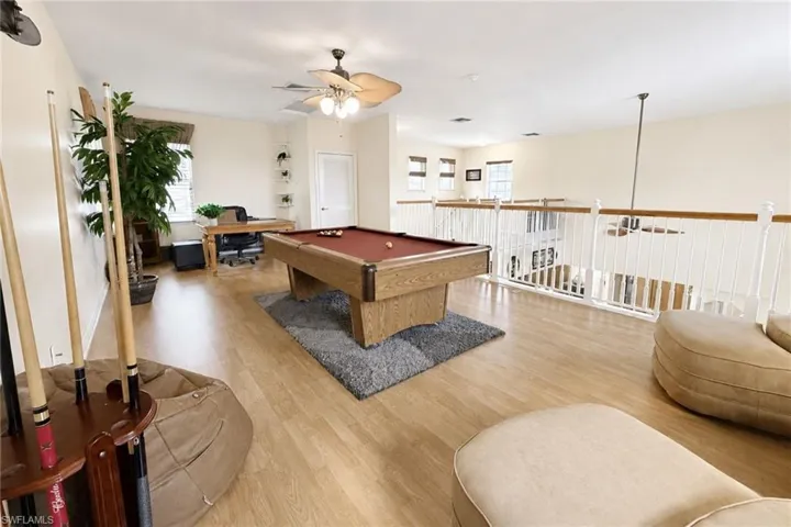 Expansive loft area featuring wood-finish flooring, white railing with wood-tone top rail, and a ceiling fan