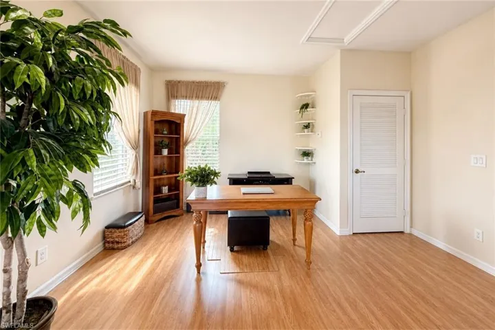 Bright room featuring wood-finish flooring, multiple windows with blinds, a louvered door, and corner shelving units