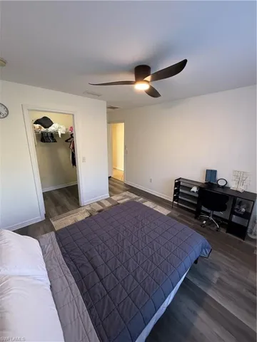 Bedroom featuring a spacious closet, dark wood-style floors, ceiling fan, and a desk