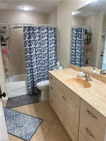 Full bath featuring vanity, a textured wall, shower / tub combo with curtain, and light tile patterned floors