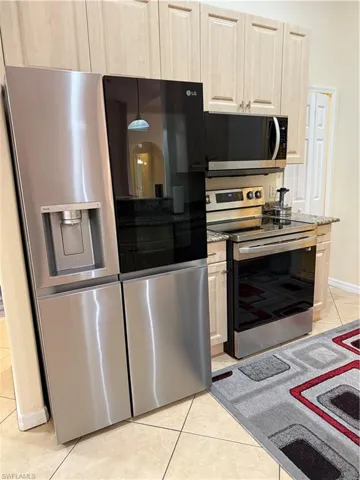 Kitchen with light tile patterned flooring, light brown cabinetry, appliances with stainless steel finishes, and light stone counters