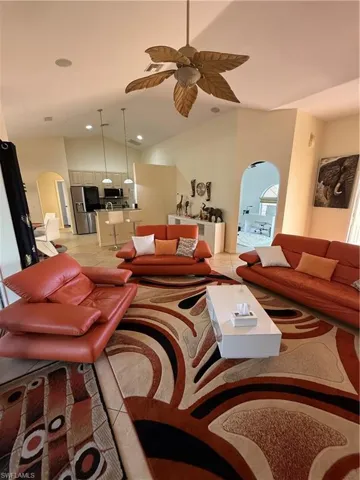Living area with arched walkways, high vaulted ceiling, light tile patterned floors, and ceiling fan