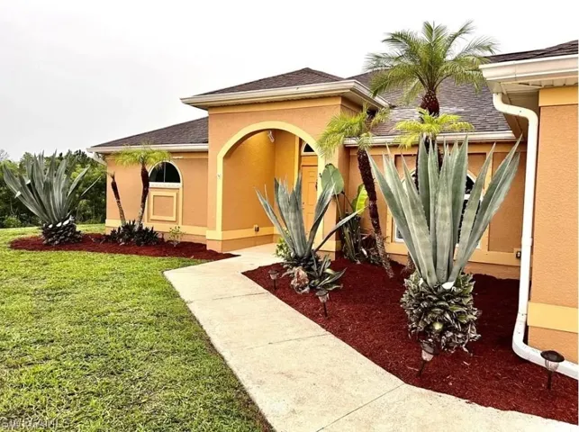 Property entrance featuring stucco siding, a lawn, and roof with shingles