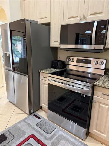 Kitchen featuring appliances with stainless steel finishes, light stone countertops, light tile patterned floors, and light brown cabinetry