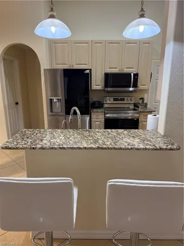 Kitchen with stove, stainless steel refrigerator, light stone counters, arched walkways, and a peninsula
