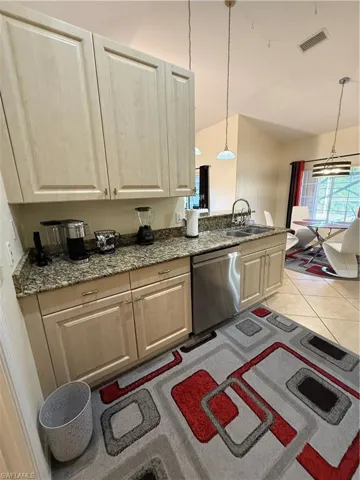 Kitchen featuring dark stone counters, lofted ceiling, dishwasher, hanging light fixtures, and light brown cabinets