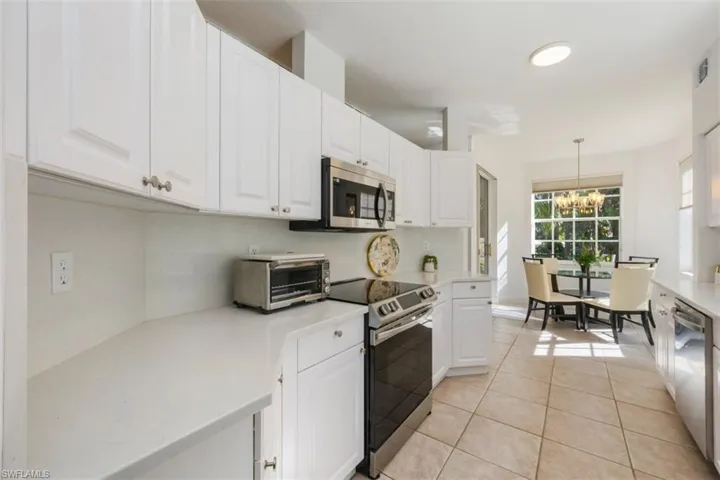 Kitchen with white cabinetry, light tile patterned flooring, appliances with stainless steel finishes, hanging light fixtures, and a chandelier